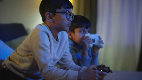 Two-Young-Boys-At-Home-Having-Fun-Playing-With-Computer-Games-Console-On-TV-Holding-Controllers-Late-At-Night-1